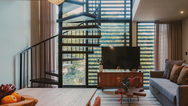 Ein modernes Wohnzimmer mit einem Holzespeisetisch, einer Couch, einem Fernseher und einer Treppe, die auf einen Balkon führt.