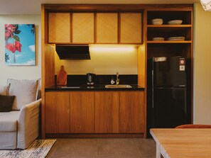 A compact kitchen with wooden cabinets, a black refrigerator, and a coffee maker. - Anandaya Sanur  (Sanur Kauh)