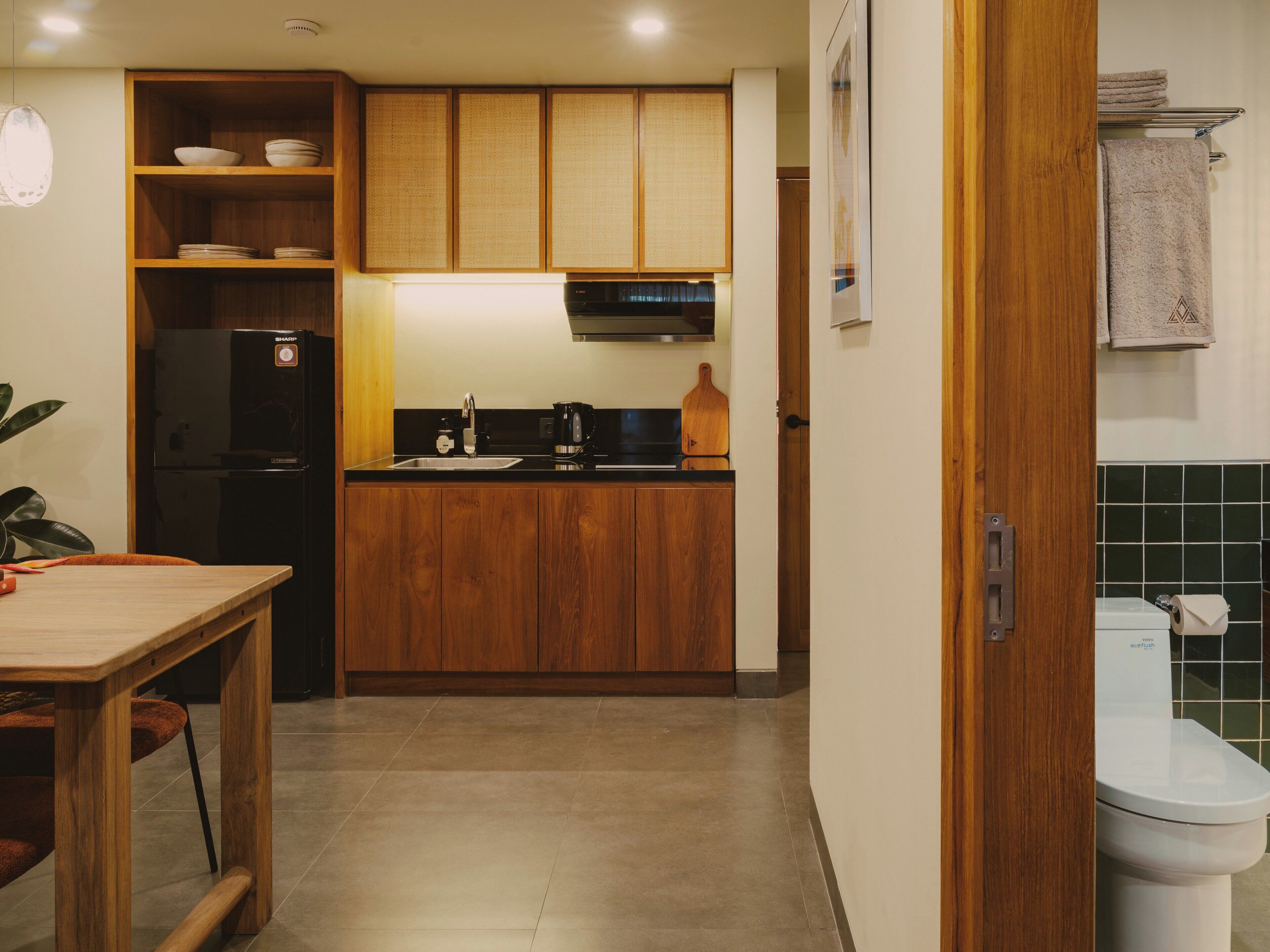 A compact kitchen with wooden cabinets, a black refrigerator, a sink, and a countertop with a kettle and a cutting board.