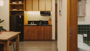 A compact kitchen with wooden cabinets, a black refrigerator, a sink, and a countertop with a kettle and a cutting board.