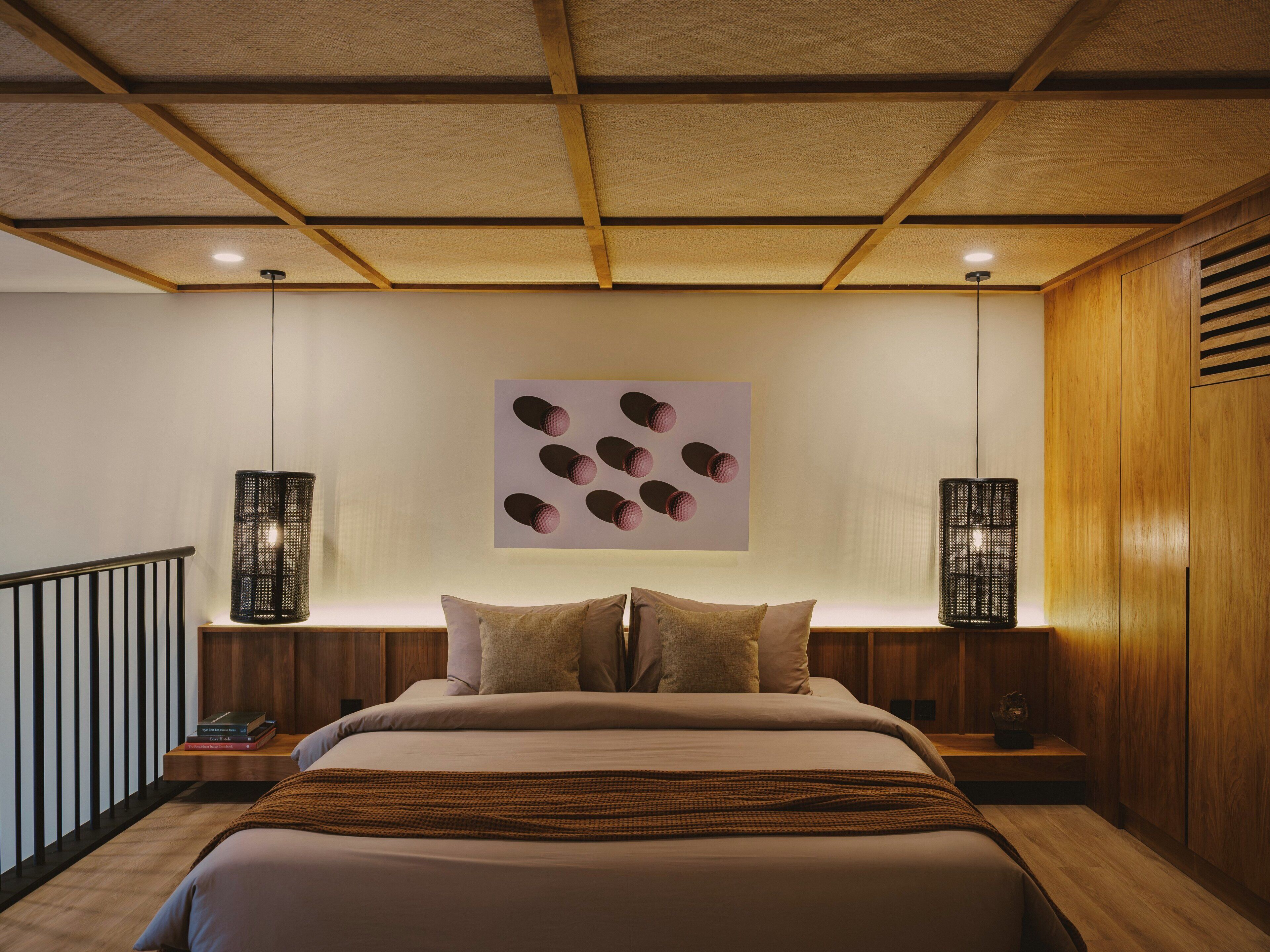 Quarto com cama, almofadas, uma obra de arte na parede e duas luminárias.