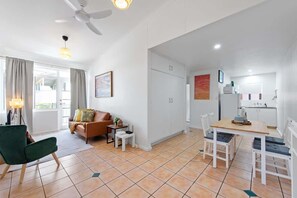 Ein modernes Wohnzimmer mit einer Couch, einem Esstisch mit Stühlen, einem Deckenventilator und einer Küchenzeile mit Schränken.