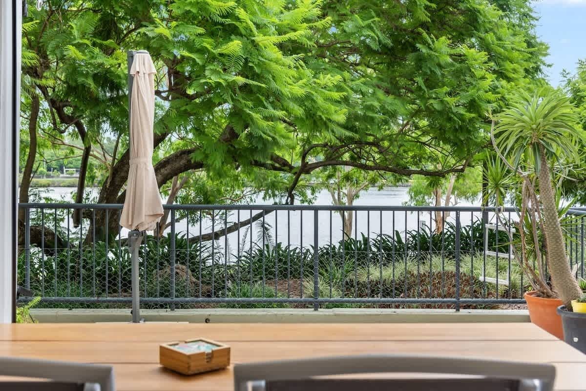 A balcony with a table, chairs, a potted plant, and a hanging umbrella.
