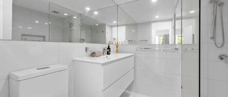 Une salle de bain moderne avec une douche à parois de verre, un meuble-lavabo blanc et un grand miroir.