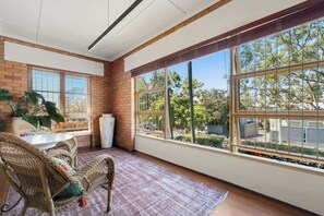 Ein sonnendurchflutetes Zimmer mit Korbmöbeln, großen Fenstern und einer Backsteinwand.