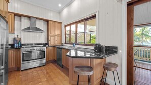 A kitchen with wooden cabinets, a stainless steel oven, a black countertop island, and a window with a view of greenery. - Comfy Character Qldr ~ 3bed House W/parking (Brisbane)