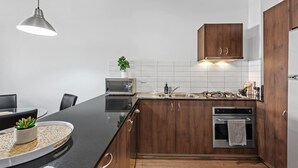 A modern kitchen with wooden cabinets, a black countertop, a microwave, an oven, and a hanging pendant light. - Hipster Loft! ~ 1bed/study/1bath/balconies/1car (Brisbane)