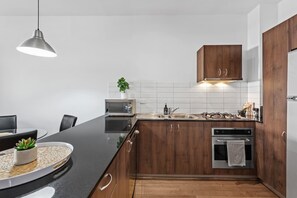 A modern kitchen with wooden cabinets, a black countertop, a microwave, an oven, and a hanging pendant light. - Hipster Loft! ~ 1bed/study/1bath/balconies/1car (Brisbane)
