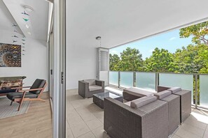 Un balcon moderne avec des meubles en osier, une rambarde en verre et une vue sur la verdure.