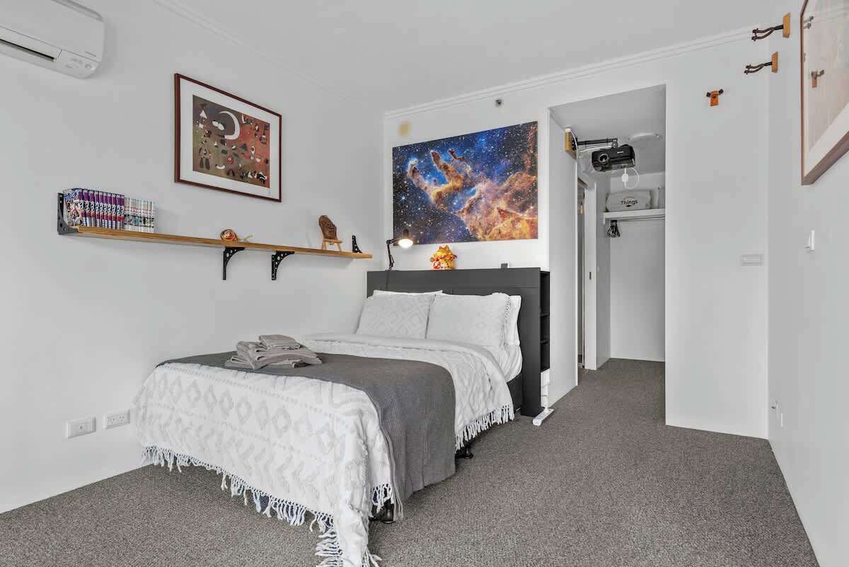 Une chambre à coucher avec un lit, une étagère remplie de livres, un tableau encadré et une grande œuvre d’art sur le th ème de l’espace accrochée au mur.