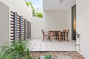 Eine Terrasse mit Tisch und Stühlen, ein Holzzaun und ein kleiner Gartenbereich mit Pflanzen und Kieselsteinen.