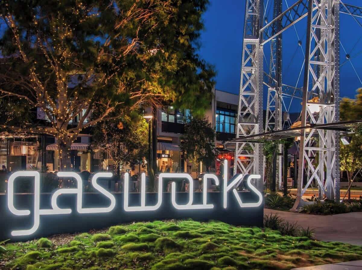 Une enseigne portant le mot « gasworks » illuminé en blanc, placée sur un fond constitué d’une structure métallique et d’arbres.