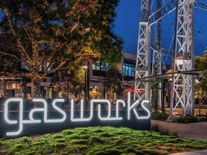 Ein Schild mit der beleuchteten Aufschrift 'gasworks' vor einer Metallkonstruktion und Bäumen.