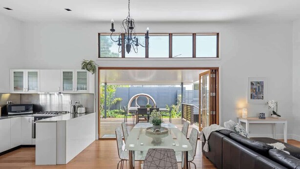 Une cuisine moderne avec un coin repas, un canapé en cuir noir et une grande fenêtre donnant sur un jardin.