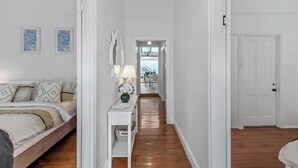 Un couloir avec un lit, une table de chevet avec une lampe et une porte donnant sur une autre pièce.