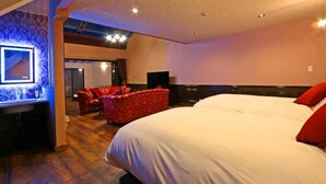 A hotel room with a large bed, a red upholstered chair, a desk with a mirror, and a flat-screen TV. - DAITO ONSEN Hotel The Ocean Hills (Kakegawa)