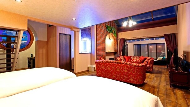 A hotel room with two beds, a red sofa, a brick accent wall, and a large window. - DAITO ONSEN Hotel The Ocean Hills (Kakegawa)