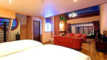 A hotel room with two beds, a red sofa, a brick accent wall, and a large window.