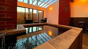 A modern indoor pool with a glass ceiling, brick walls, and a seating area. - DAITO ONSEN Hotel The Ocean Hills (Kakegawa)