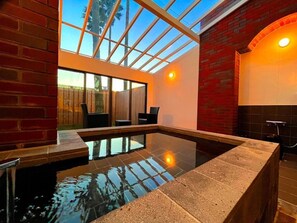 A modern indoor pool with a glass ceiling, brick walls, and a seating area. - DAITO ONSEN Hotel The Ocean Hills (Kakegawa)