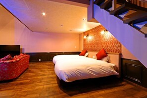 A bedroom with a bed, a red sofa, a TV, and a staircase. - DAITO ONSEN Hotel The Ocean Hills (Kakegawa)