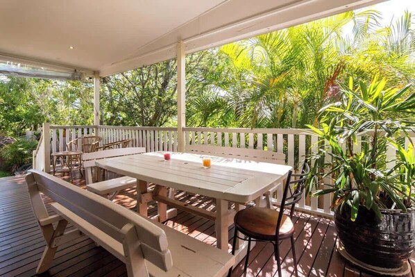 A covered outdoor patio with a wooden table and chairs, surrounded by a white fence and lush greenery. - Spacious 4 Bedroom House - Walk to Southbank (Brisbane)