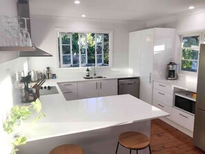 A modern kitchen with white cabinetry, a large island, and a window with a view of greenery. - Spacious 4 Bedroom House - Walk to Southbank (Brisbane)