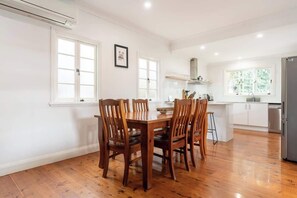A dining area with a wooden table and chairs, a kitchen with white cabinets, and a refrigerator.