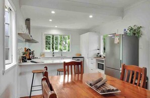 A modern kitchen with white cabinets, a wooden dining table, and a stainless steel refrigerator. - Spacious 4 Bedroom House - Walk to Southbank (Brisbane)