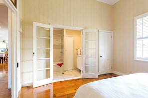 A bedroom with a wooden floor, a bed, a closet with a sliding door, and a bathroom with a shower and toilet.