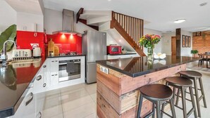 Una cocina moderna con una isla central, electrodomésticos de acero inoxidable y una escalera de madera.