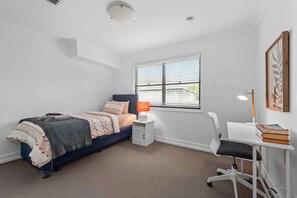 Une chambre à coucher avec un lit, une table de chevet, une chaise et une fenêtre avec des stores.