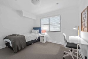 Une chambre à coucher comprenant un lit, une table de chevet, une lampe, un bureau, une chaise et une fenêtre.