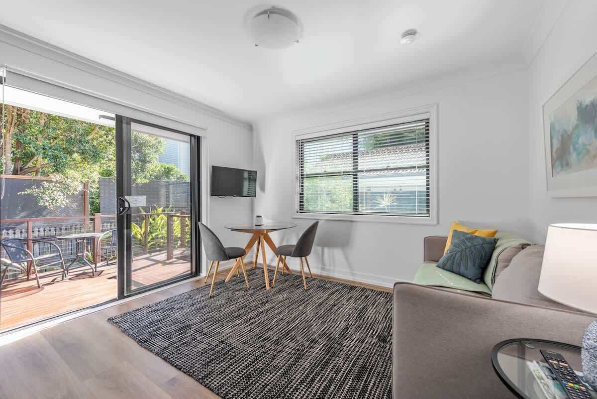 A modern living room with a sliding glass door leading to an outdoor area, a flat-screen TV mounted on the wall, and a cozy seating area with a sofa and a coffee table.