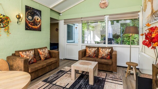 Sala de estar com dois sofás, uma mesa de centro, um relógio de parede e uma janela com vista para o verde.