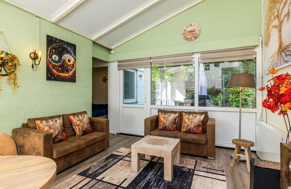 Ein Wohnzimmer mit zwei Sofas, einem Couchtisch, einer Wanduhr und einem Fenster mit Blick auf Grünflächen.