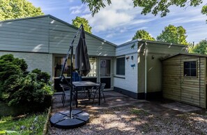 Eine Terrasse mit Tisch und Stühlen, ein kleines Gartenhaus und ein Haus mit Fenster und Tür.