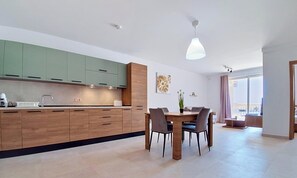 A modern kitchen with wooden cabinets, a dining table with chairs, and a pendant light. - Modern 2BR Flat · Balcony · St Paul's Bay (San Pawl il-Baħar)