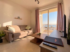 A modern living room with a sofa, a coffee table, a TV, and a balcony with a view. - Modern 2BR Flat · Balcony · St Paul's Bay (San Pawl il-Baħar)