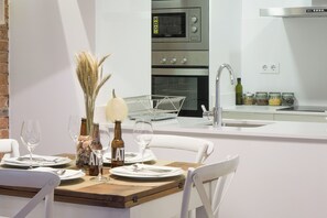 Una cocina moderna con horno empotrado, un lavaplatos y una zona de comedor con mesa de madera dispuesta para dos personas.