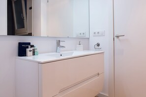 Un baño moderno con un lavabo, espejo y armarios blancos.