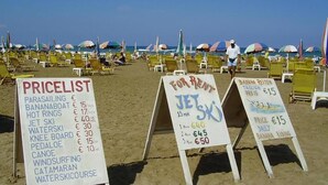 Beachside chairs, umbrellas, and signs advertising water sports and rental prices.
