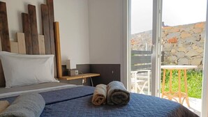 A bedroom with a bed, a wooden headboard, a small table, and a balcony with a stone wall and a chair.