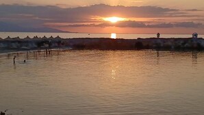A sunset over a calm body of water with a rocky shoreline and a few people in the distance.