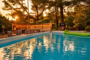 A swimming pool with a basketball hoop, surrounded by trees and a covered area with seating. - Wooden house / Swimming pool / Private Guinguette / Sea view / Air conditioning / Jacuzzi optional (Le Beausset)