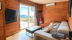 En inredning med träpanel, en soffa, ett bord, en tv och en skjutdörr i glas som leder ut till ett utomhusområde.