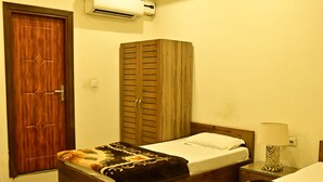 Un dormitorio con dos camas, ventilador de techo, aire acondicionado, armario de madera y una lámpara de noche.
