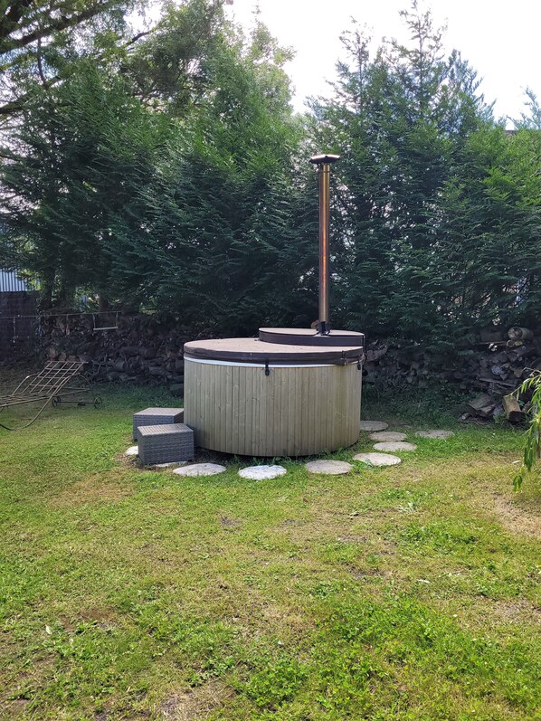 Un jacuzzi en un patio trasero con un muro de piedra, una silla de metal y una terraza de madera.