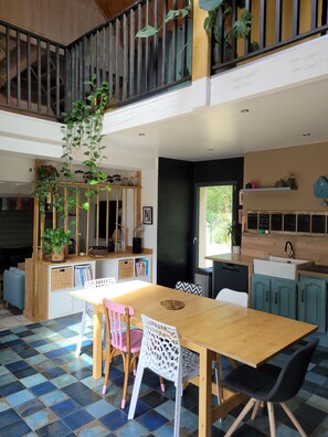 Un comedor amplio con mesa y sillas de madera, una cocina con armarios color turquesa y un balcón con plantas.
