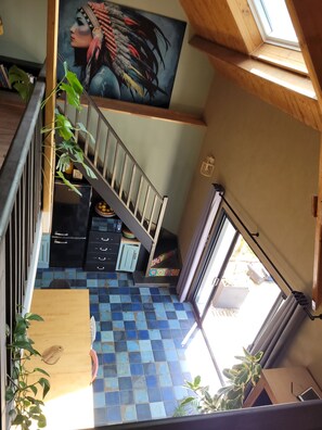 Un escalier offrant une vue sur une pièce dotée d’un sol carrelé, d’un tableau et d’une fenêtre.